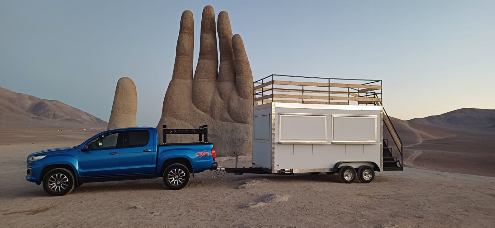 Food truck 2x4 metros con terraza posando frente a la escultura de mano en el desierto de Atacama